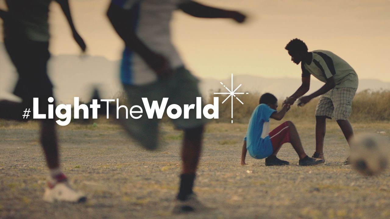En gutt hjelper en annen gutt å reise seg etter å ha falt mens han spilte fotball, fra videoen Lys for verden